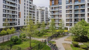 Ein moderner Wohnkomplex mit mehreren Balkonen, einem zentralen Innenhof mit Bäumen und einem Fahrradstellplatz.