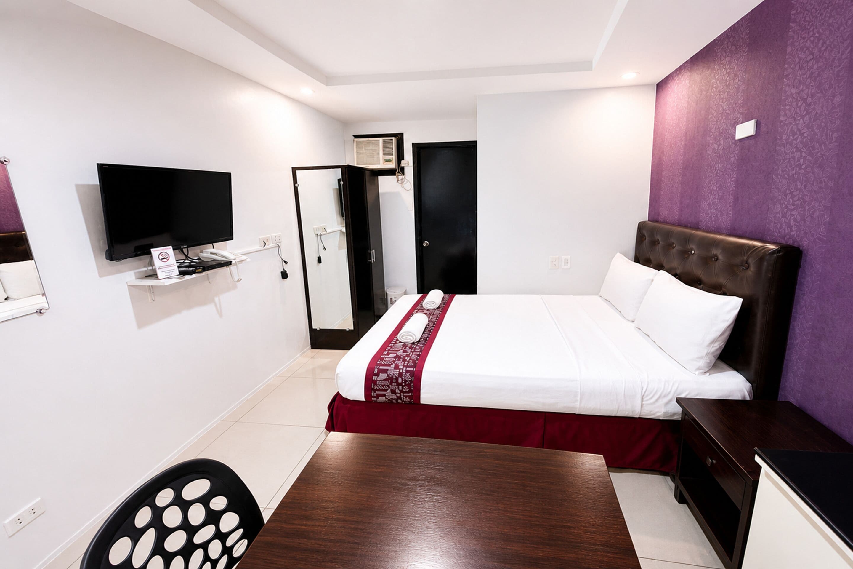 Quarto de hotel com uma cama, uma televisão, uma escrivaninha e uma cadeira.