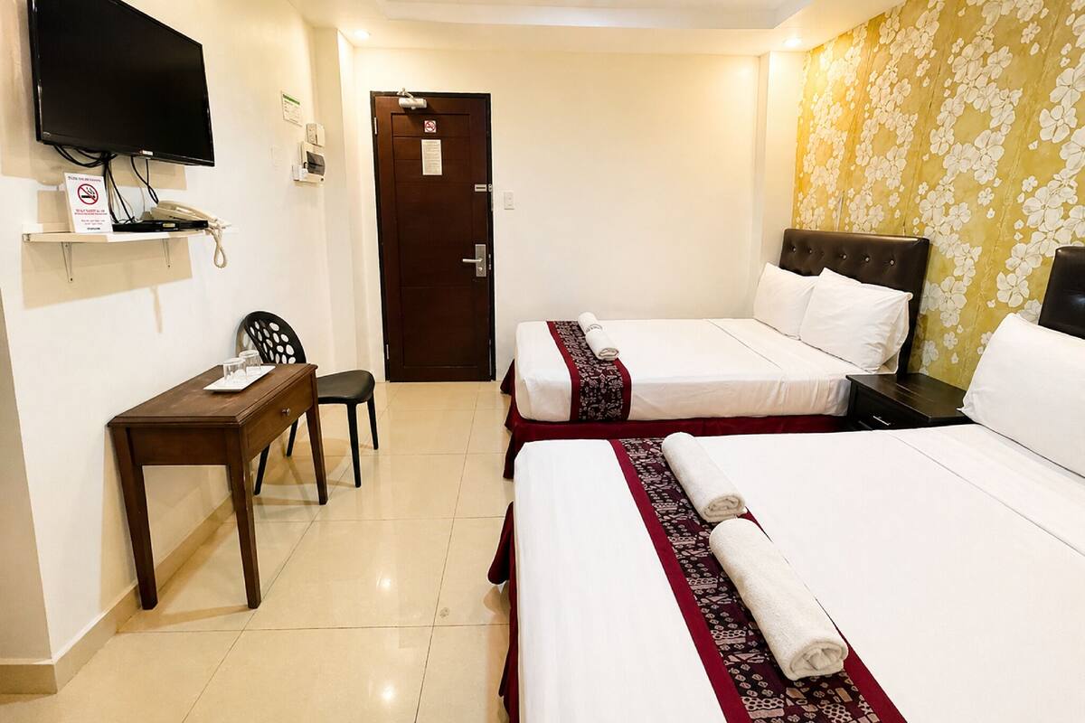 A hotel room with two beds, a desk, a chair, a television, and a door.