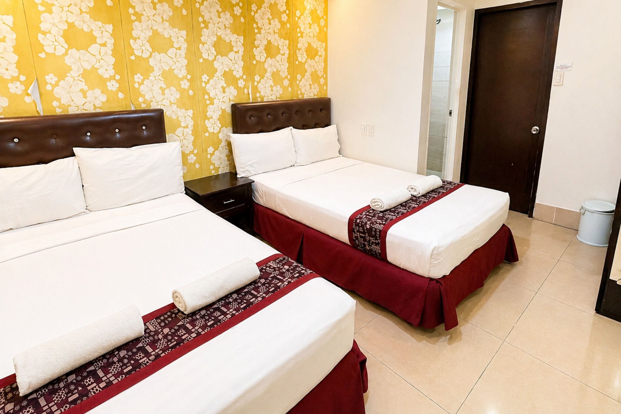 A hotel room with two beds, a wooden headboard, a patterned wall, and a door.
