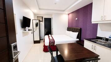 A hotel room with a bed, a desk, a chair, a television, a wardrobe, and a kitchenette.
