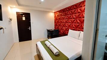 A hotel room with a bed, a desk, and a red geometric wall.