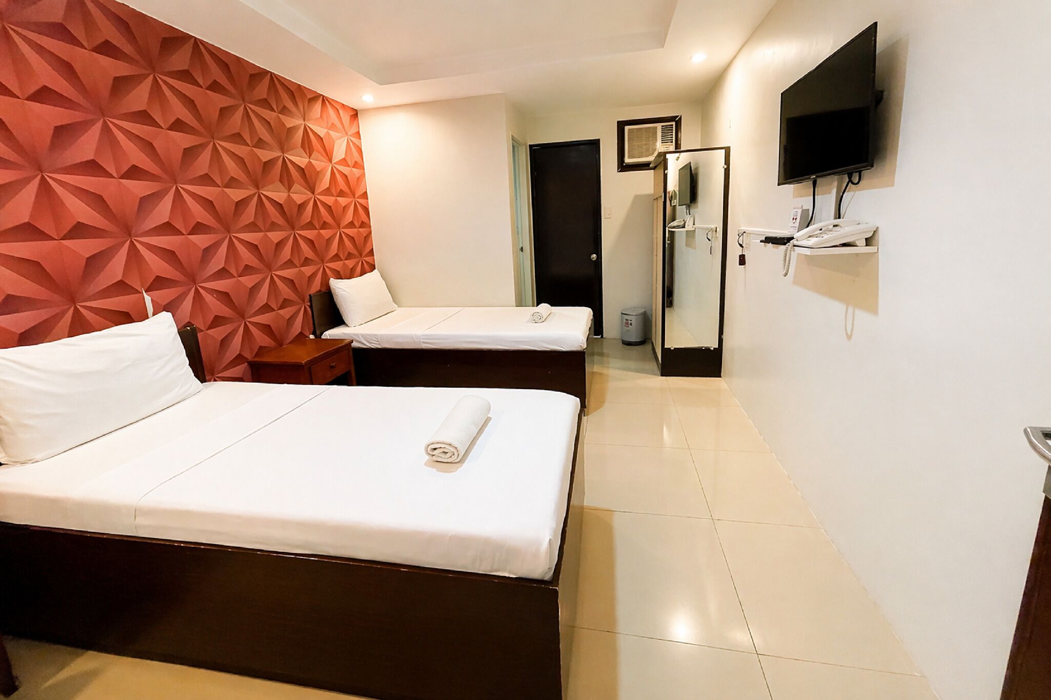 A hotel room with two beds, a TV, a minibar, and a door leading to a bathroom.
