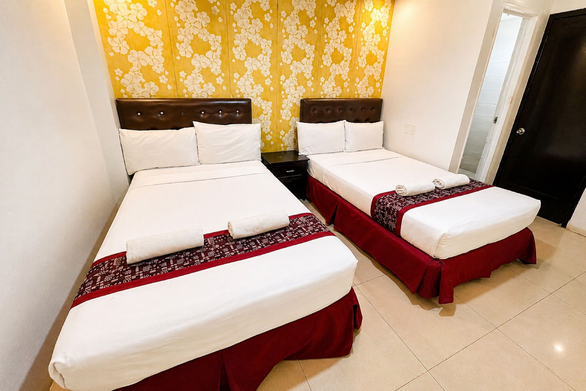 A hotel room with two beds, a wooden headboard, a patterned wall, and a door.