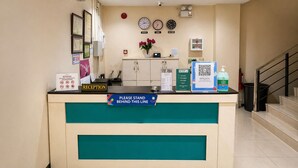 A reception desk with a 'RECEPTION' sign, a 'PLEASE STAND BEHIND THIS LINE' sign, a clock, and a QR code for Google Maps. - Obrero Suites Davao (Davao)