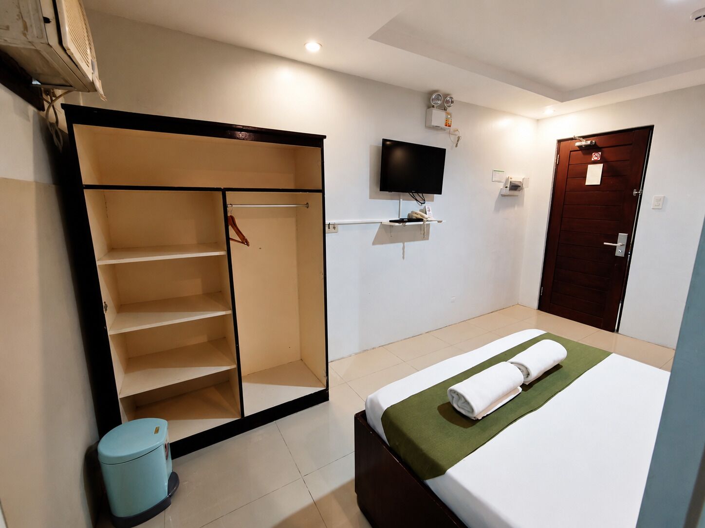 A hotel room with a bed, a wardrobe, a television, and a door.