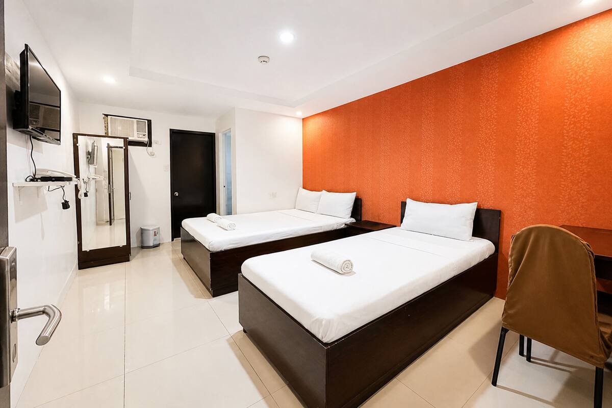 A hotel room with two beds, a TV, a desk, and a chair.