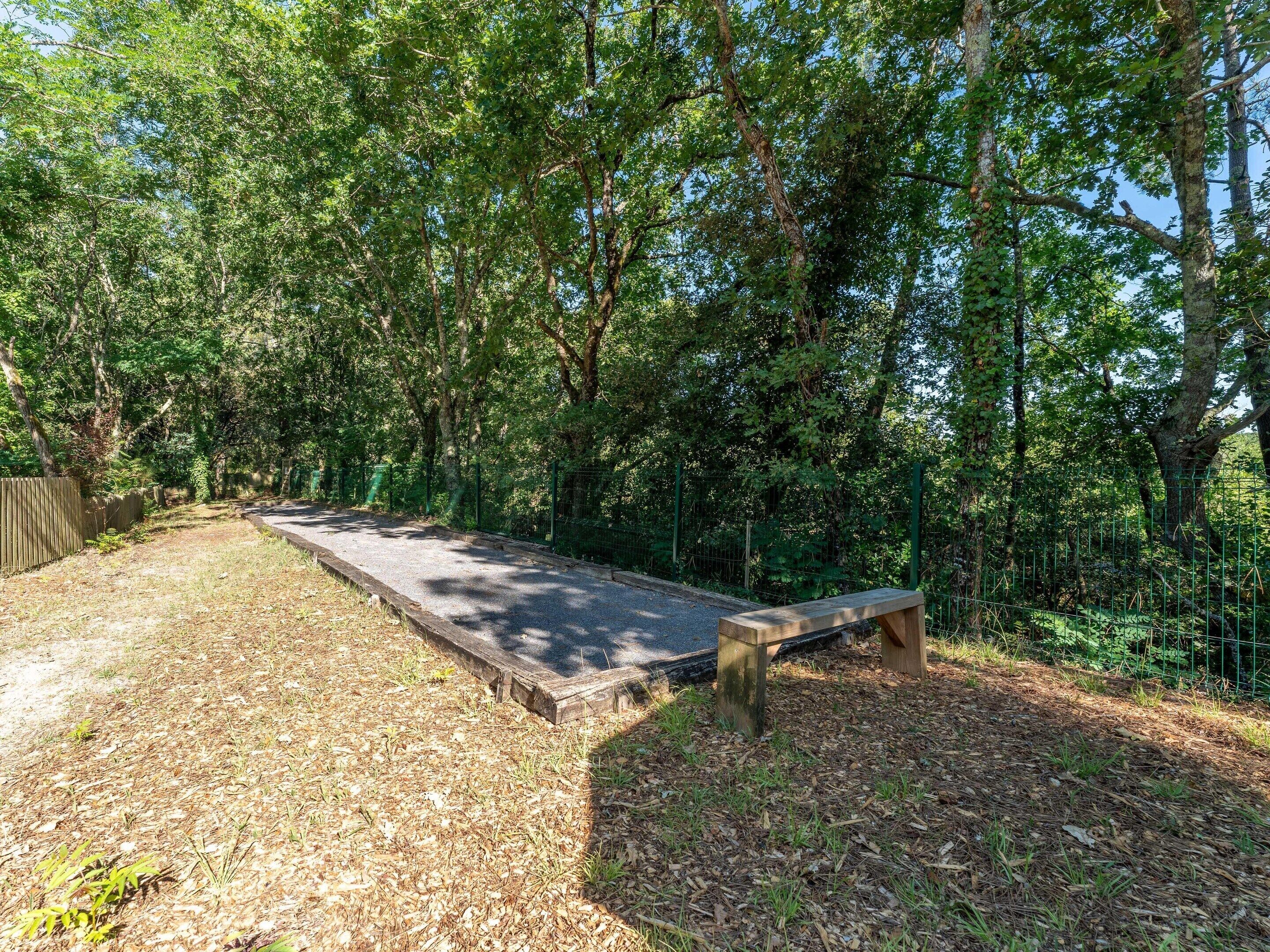 A bench in a wooded area with a dirt path and a fence.