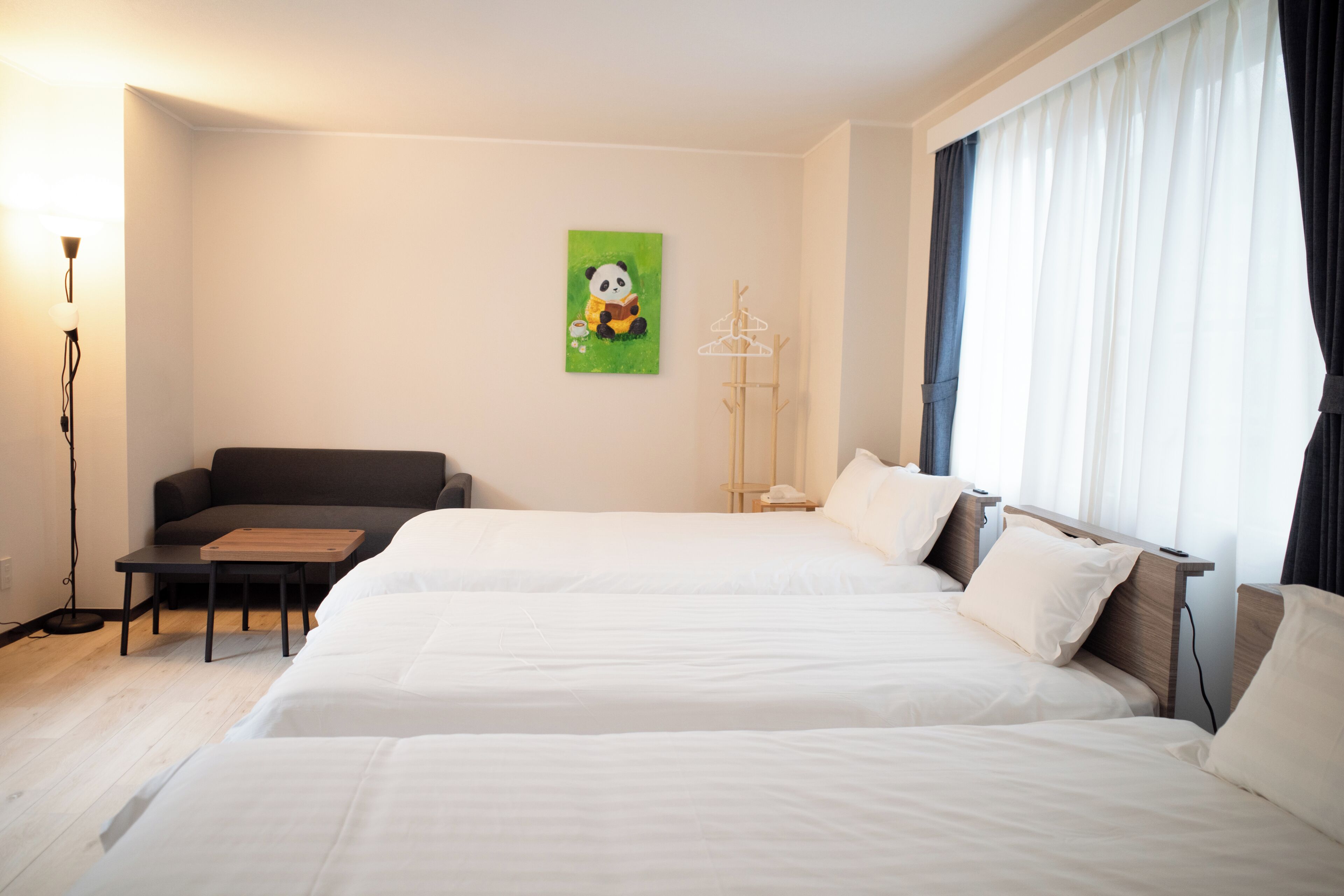A hotel room with two beds, a sofa, a small table, a lamp, and a painting on the wall.