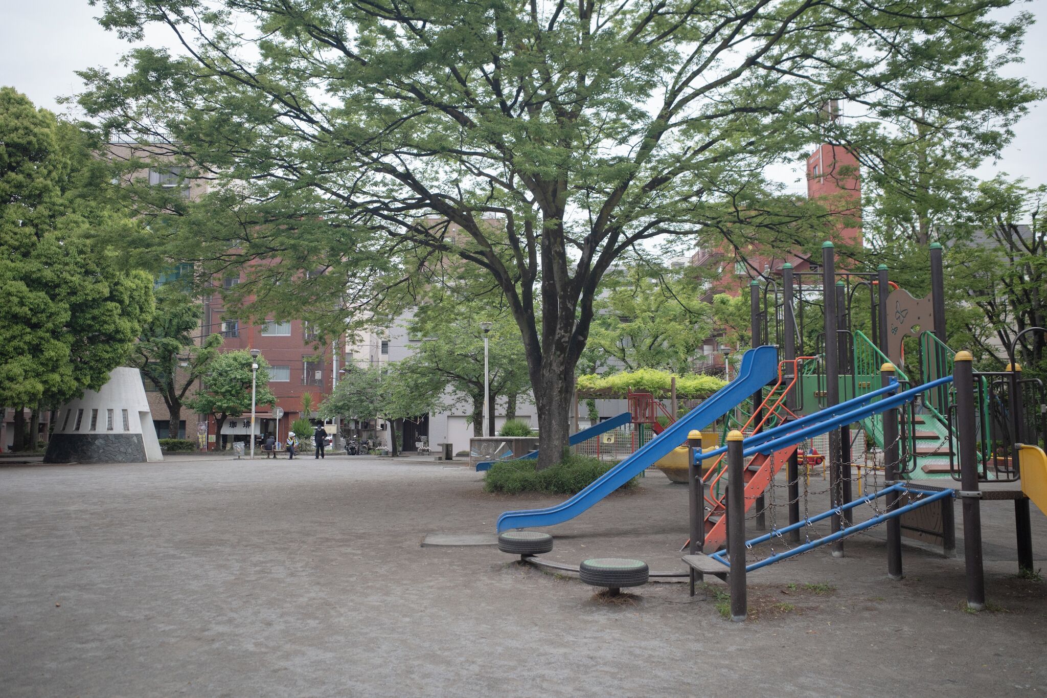 A playground with slides and climbing structures, surrounded by trees and buildings.
