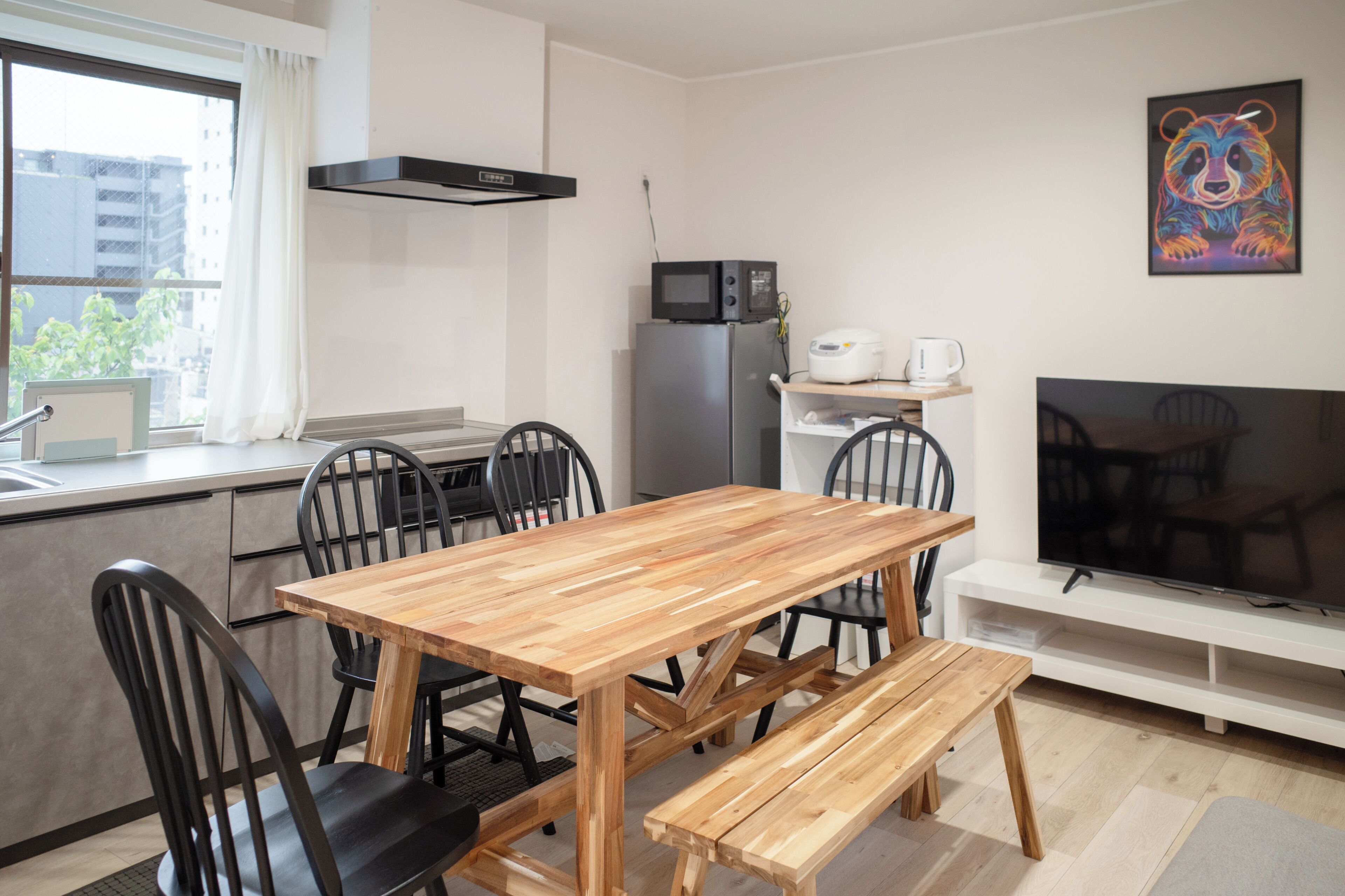 A modern kitchen with a wooden table and chairs, a microwave, refrigerator, and a TV.