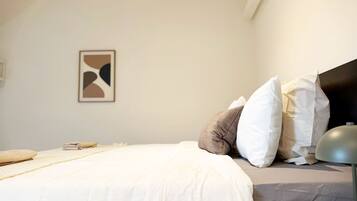 A neatly made bed with a white comforter and pillows, a bedside lamp, and a framed abstract artwork on the wall.