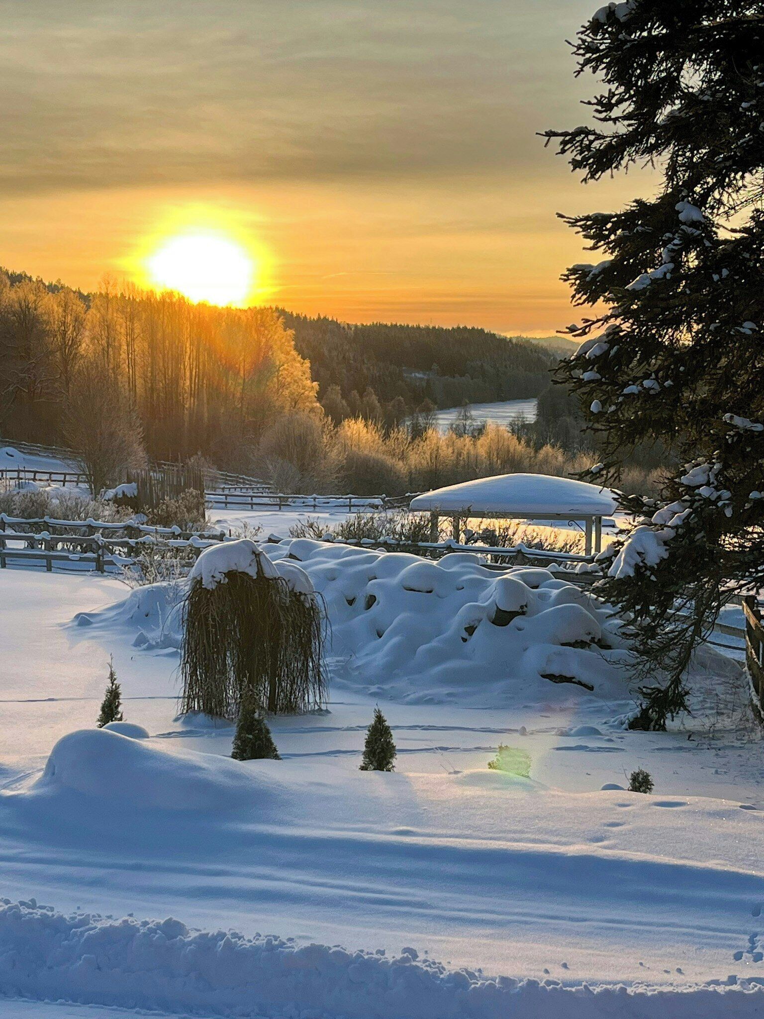 Un paisaje nevado con cielo iluminado por el sol, un campo cubierto de nieve y una estructura de madera.