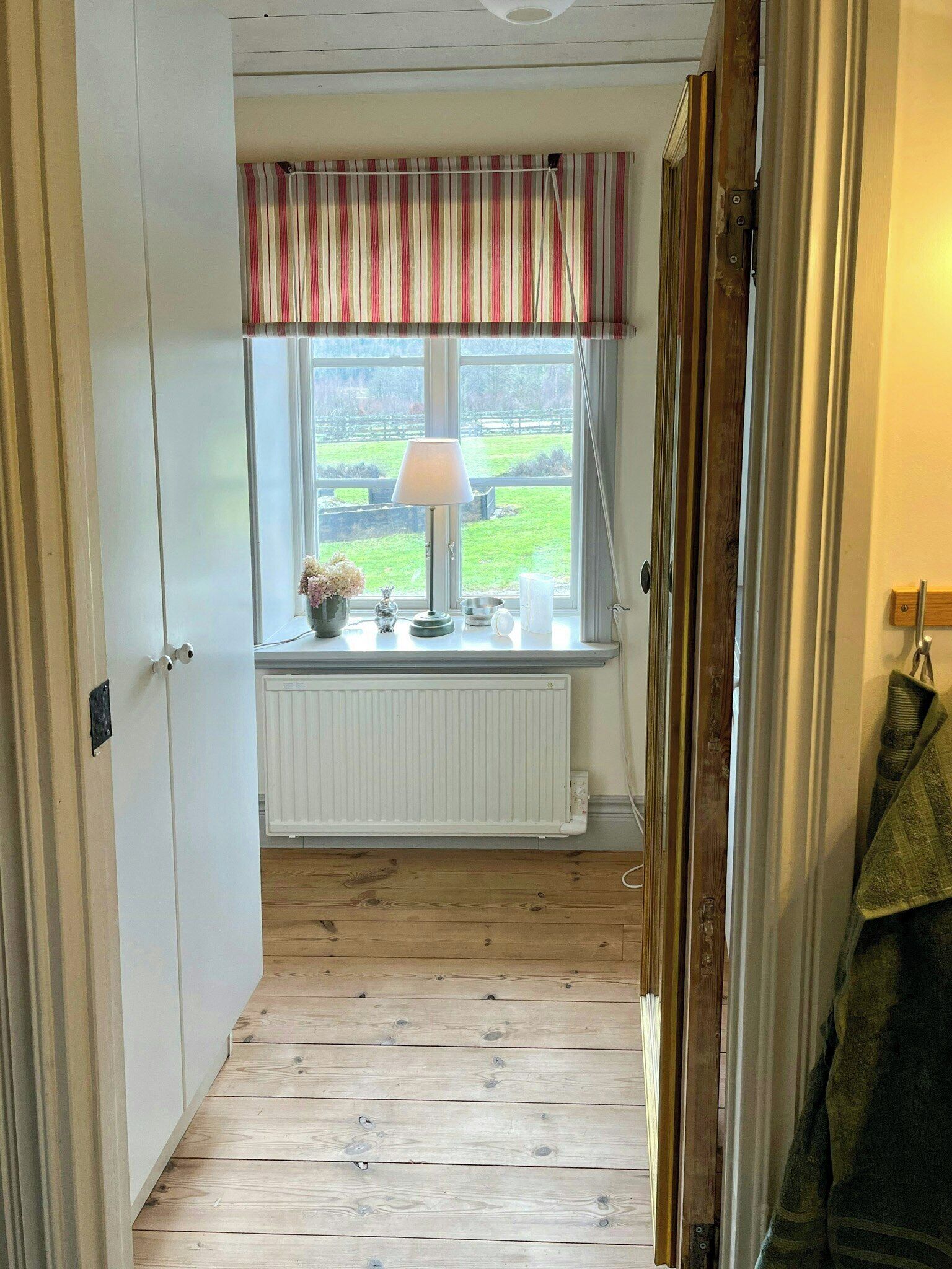 A narrow hallway with a window, radiator, and a lamp on a table.