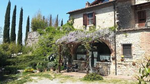 A rustic stone building with a garden patio, a pergola with climbing plants, and a view of tall trees. - Villa with private pool among Siena's olive groves (Rapolano Terme)