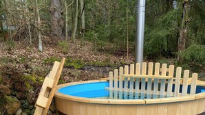 A wooden hot tub with a glass edge, a wooden bench, and a small table.