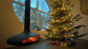 A Christmas tree with lights, a fireplace, and a window with a view of trees.