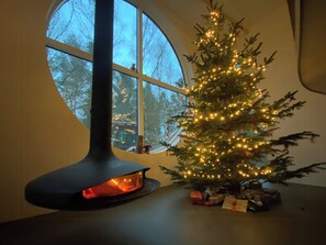 Árvore de Natal iluminada, lareira e janela com vista para árvores.