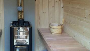 Una sauna con un calentador negro, un banco de madera y un balde.