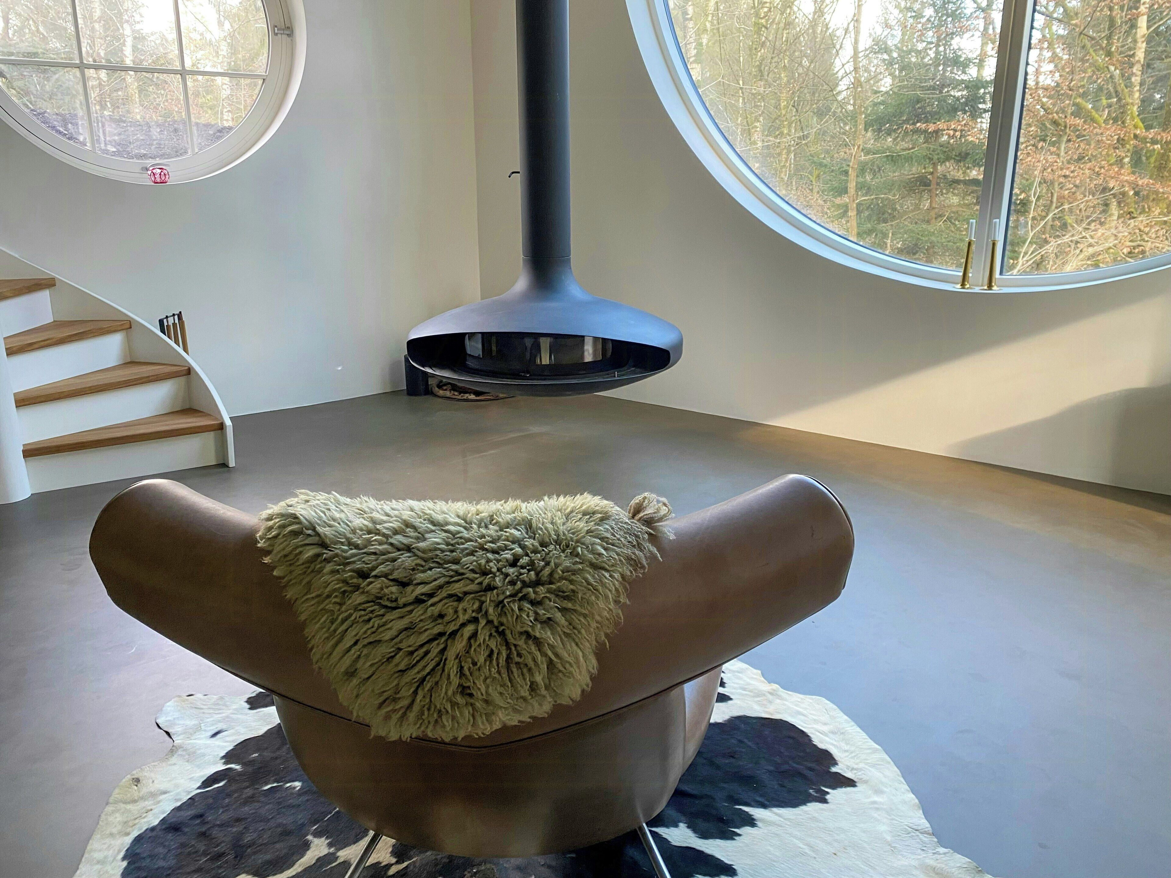 Et moderne interiør med et unikt loftdesign, et rundt vindue og udsigt til træer.