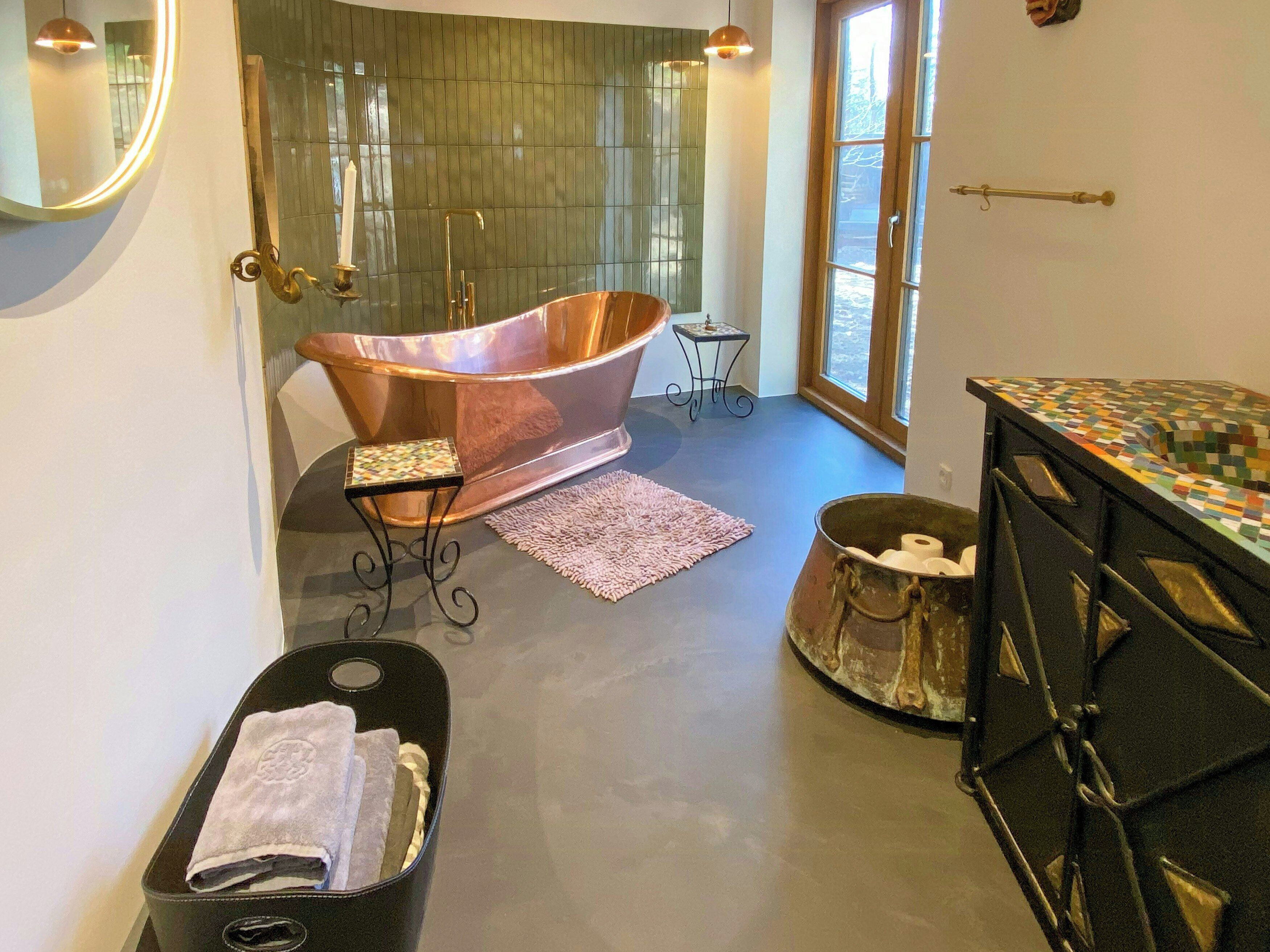 Une salle de bain moderne avec une baignoire sur pieds, un meuble-lavabo surmonté d'un plan en mosaïque, un petit tabouret et une grande fenêtre.