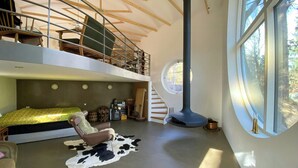 A loft-style room with a bed, a leather chair, a cowhide rug, a large window, and a tall chimney.