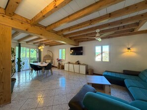 A spacious living area with a wooden ceiling, a sofa, a dining table with chairs, and a TV mounted on the wall. - La Maison d'Artzamendi - Mountain view (LOUHOSSOA)