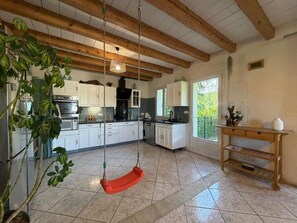 A kitchen with white cabinets, a hanging orange swing, and a wooden table with a vase. - La Maison d'Artzamendi - Mountain view (LOUHOSSOA)