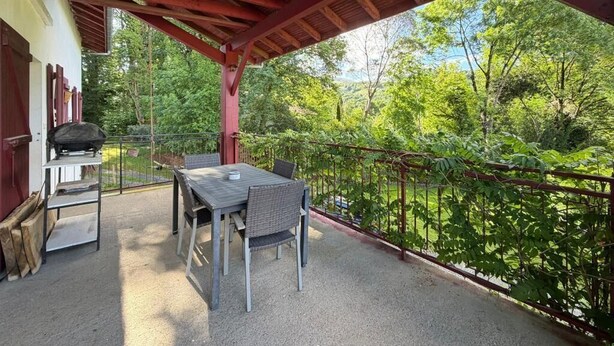 Patio esterno con tavolo e sedie, un barbecue e vista su una zona boschiva.