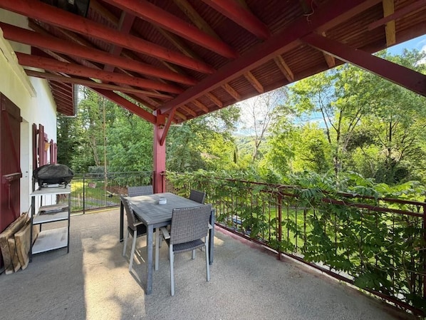 An outdoor patio with a table and chairs, a grill, and a view of a forested area. - La Maison d'Artzamendi - Mountain view (LOUHOSSOA)