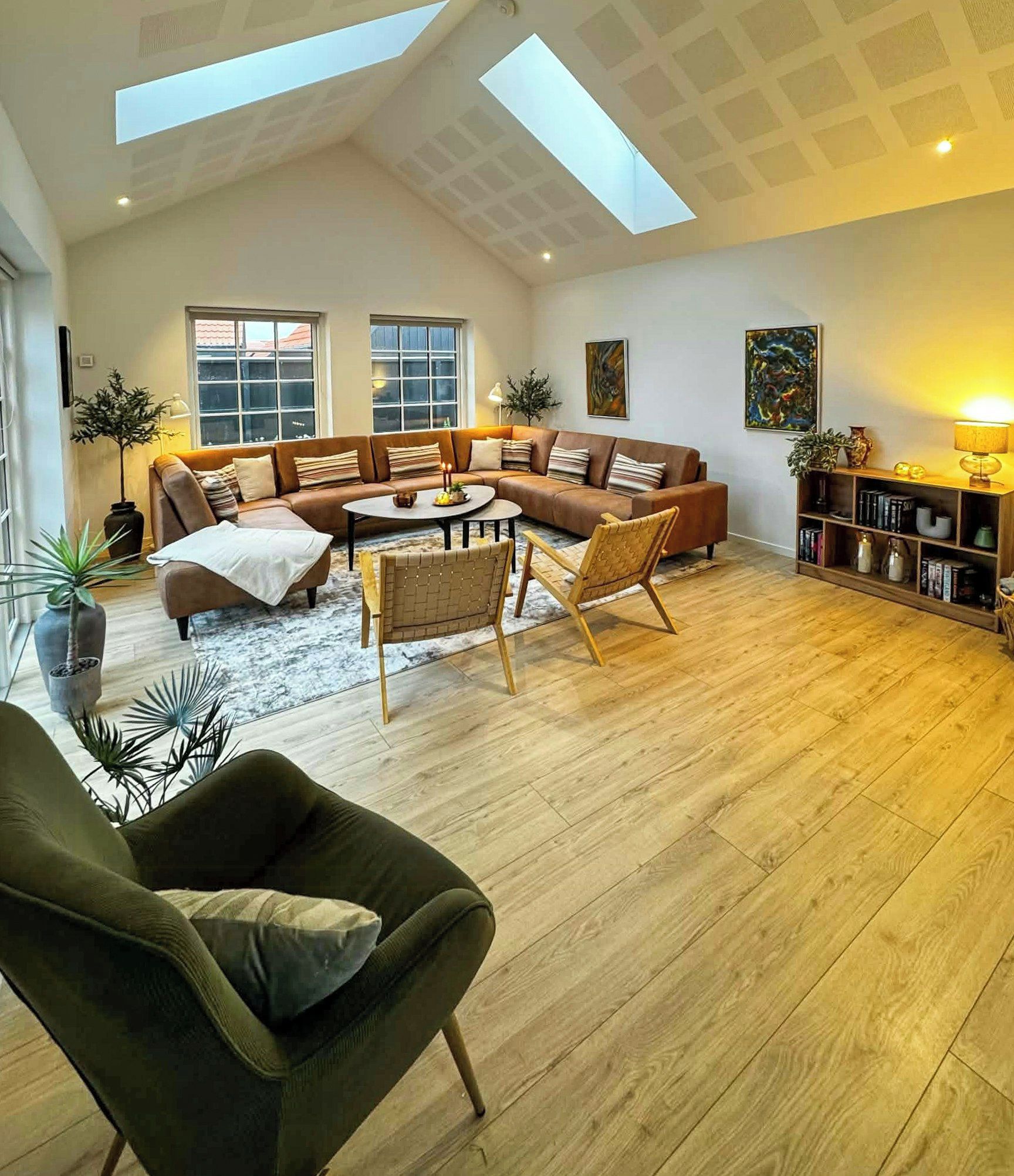 A spacious living room with a high ceiling, a sectional sofa, a coffee table, and a bookshelf.