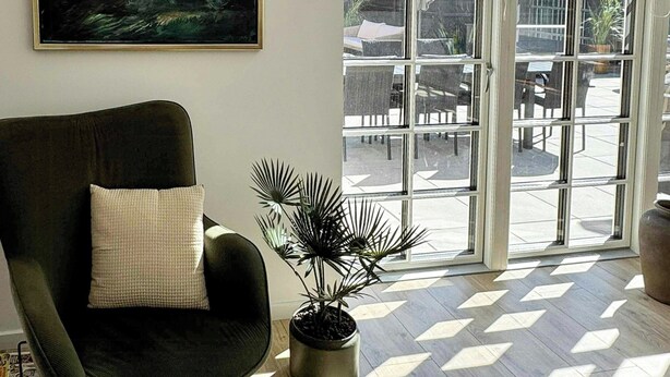 Una habitación con un sillón negro, una planta en maceta, un cuadro enmarcado y un ventanal con vistas al exterior.