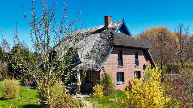 Ein traditionelles Haus mit Strohdach, Backsteinmauern und einem kleinen Balkon.