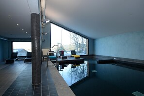 Piscina interna con vista sulle montagne, sedie a sdraio e pavimento piastrellato.