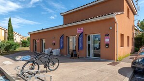 Um edifício com área de recepção, uma bicicleta estacionada na frente e um carro por perto.