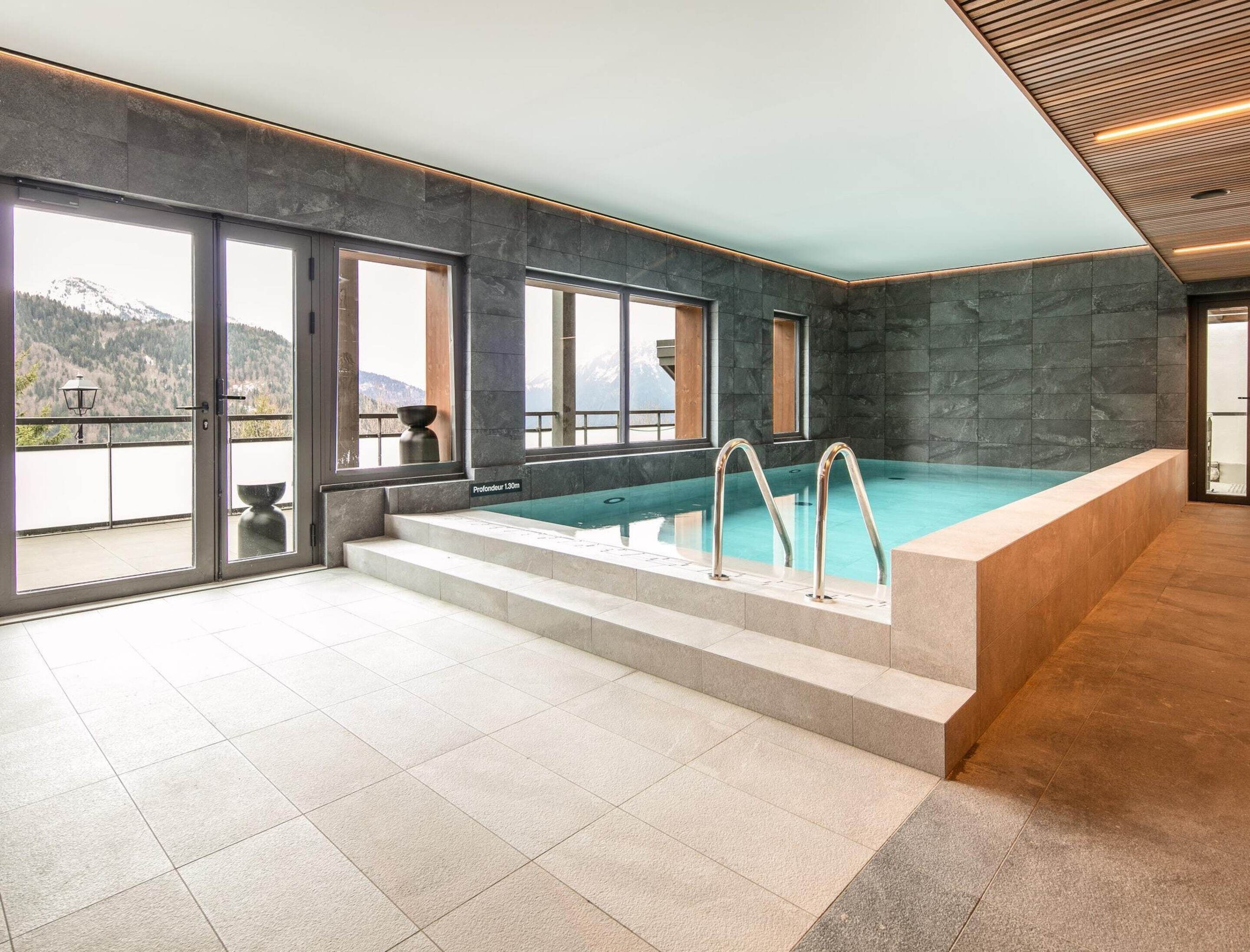 An indoor swimming pool with a view of mountains, stone walls, and a tiled floor.