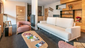 Un soggiorno moderno con un divano, un tavolino con riviste, una sedia in legno, un frigorifero e una parete di legno con mensole.