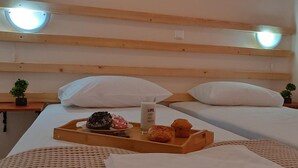 Ett hotellrum med två sängar, sänggavlar i trä, nattduksbord med krukväxter, ett bricka med frukosttillbehör och en sänglampa.