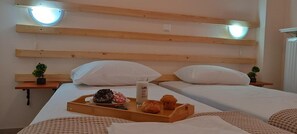 A hotel room with two beds, wooden headboards, bedside tables with potted plants, a tray with breakfast items, and a bedside lamp.