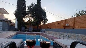En avslappnad miljö vid poolen med två glas rött vin, en fruktskål och solstolar.