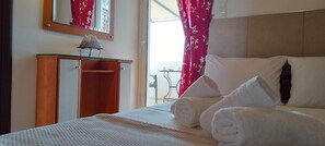 A hotel room with a bed, a bedside table with a lamp, a mirror, and a window with curtains. - Studio Apartment with Sea View and 2 Balconies (Kato Loutro)