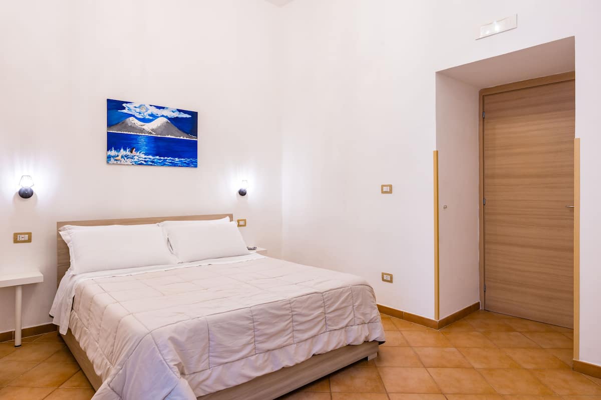 A bedroom with a bed, a wall-mounted painting, bedside lamps, and a wooden door.