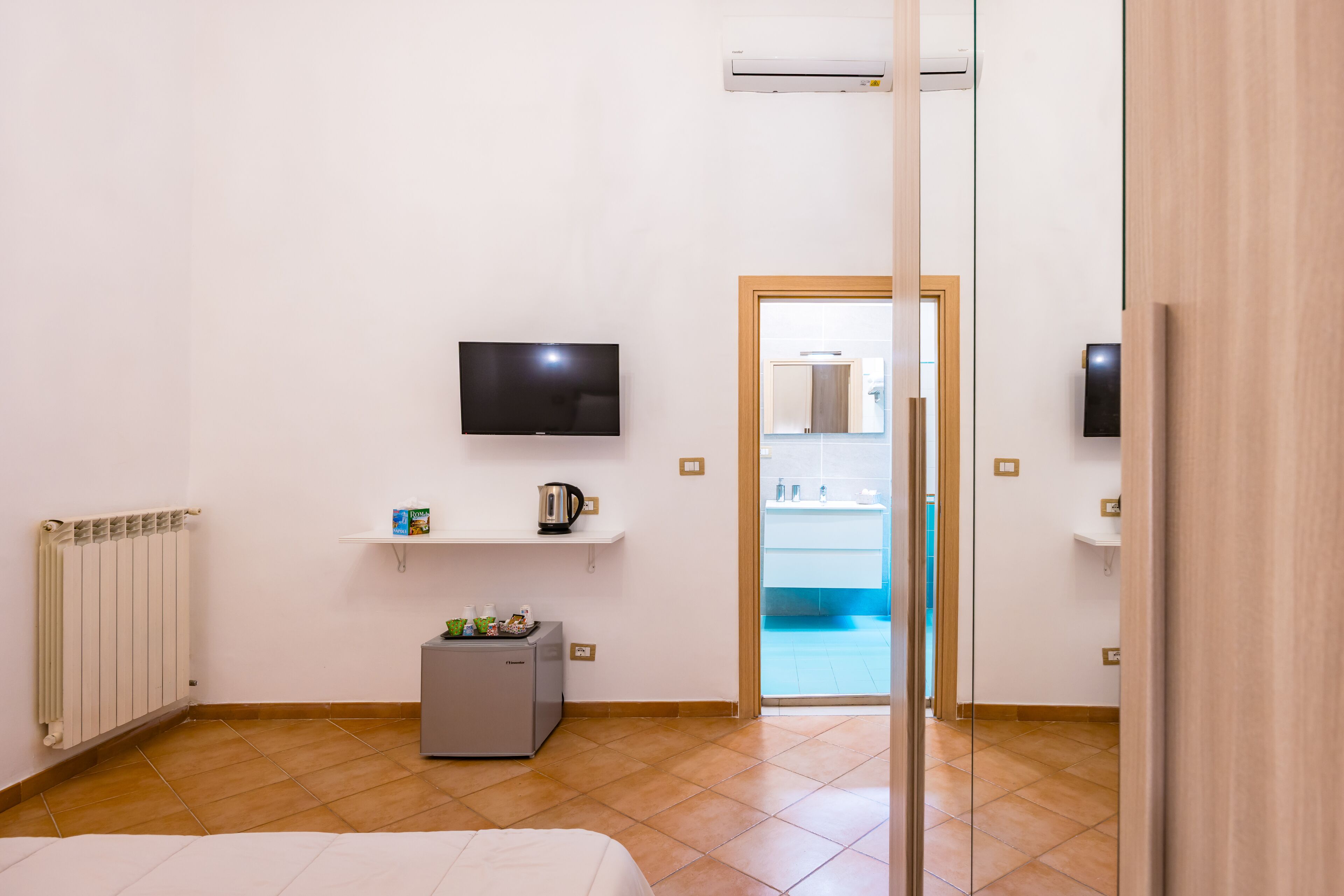 A hotel room with a bed, a TV, a small kitchenette, and a view of the pool.
