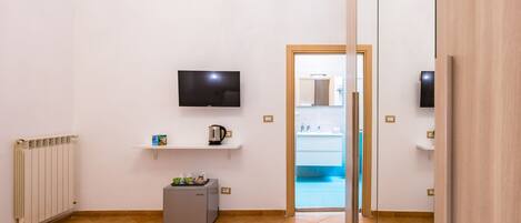 A hotel room with a bed, a TV, a small kitchenette, and a view of the pool.