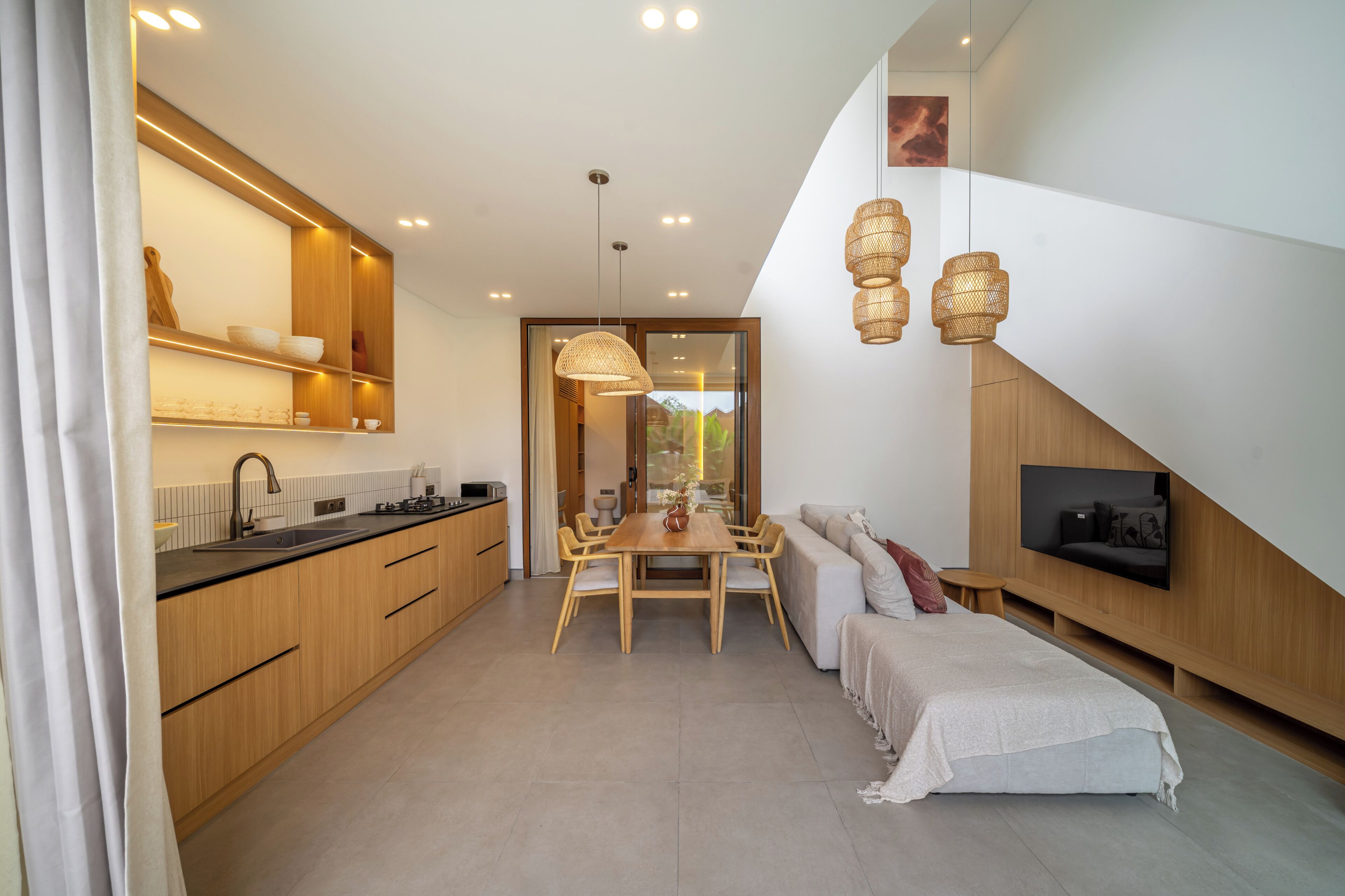 Una cocina moderna con armarios de madera, un comedor con mesa y sillas, un sofá y un televisor montado en la pared.