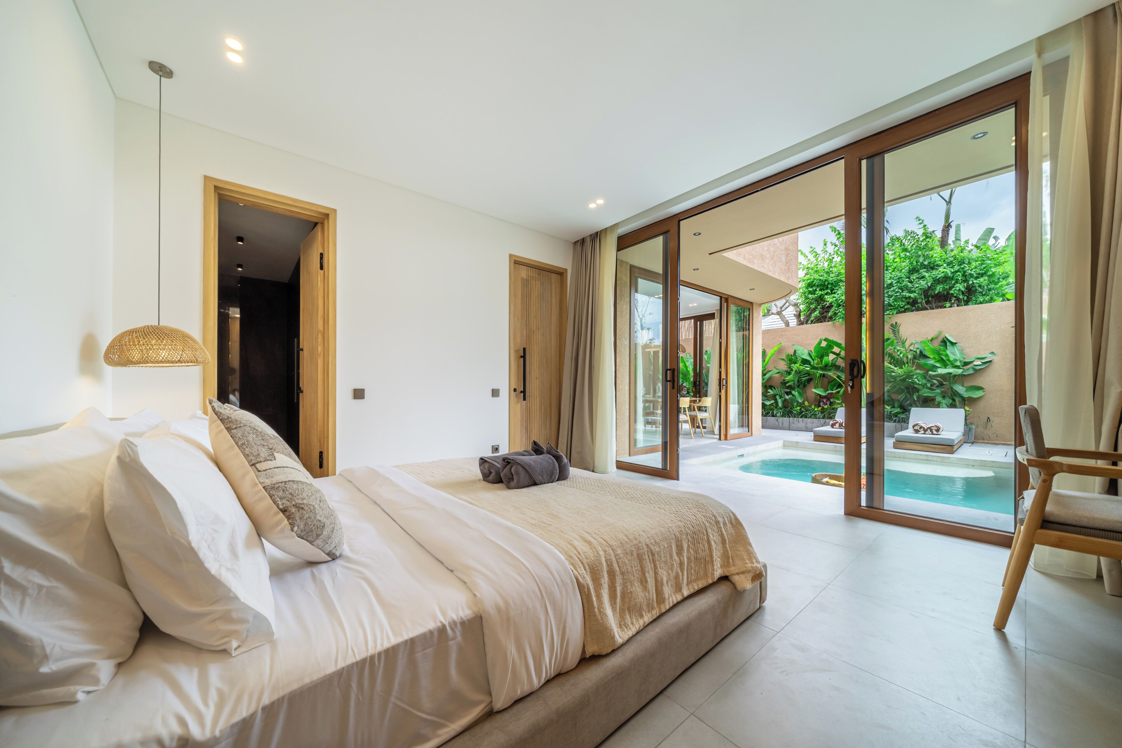 Une chambre dotée d’un grand lit, offrant une vue sur une piscine, et donnant sur un espace extérieur grâce à des portes-fenêtres coulissantes.