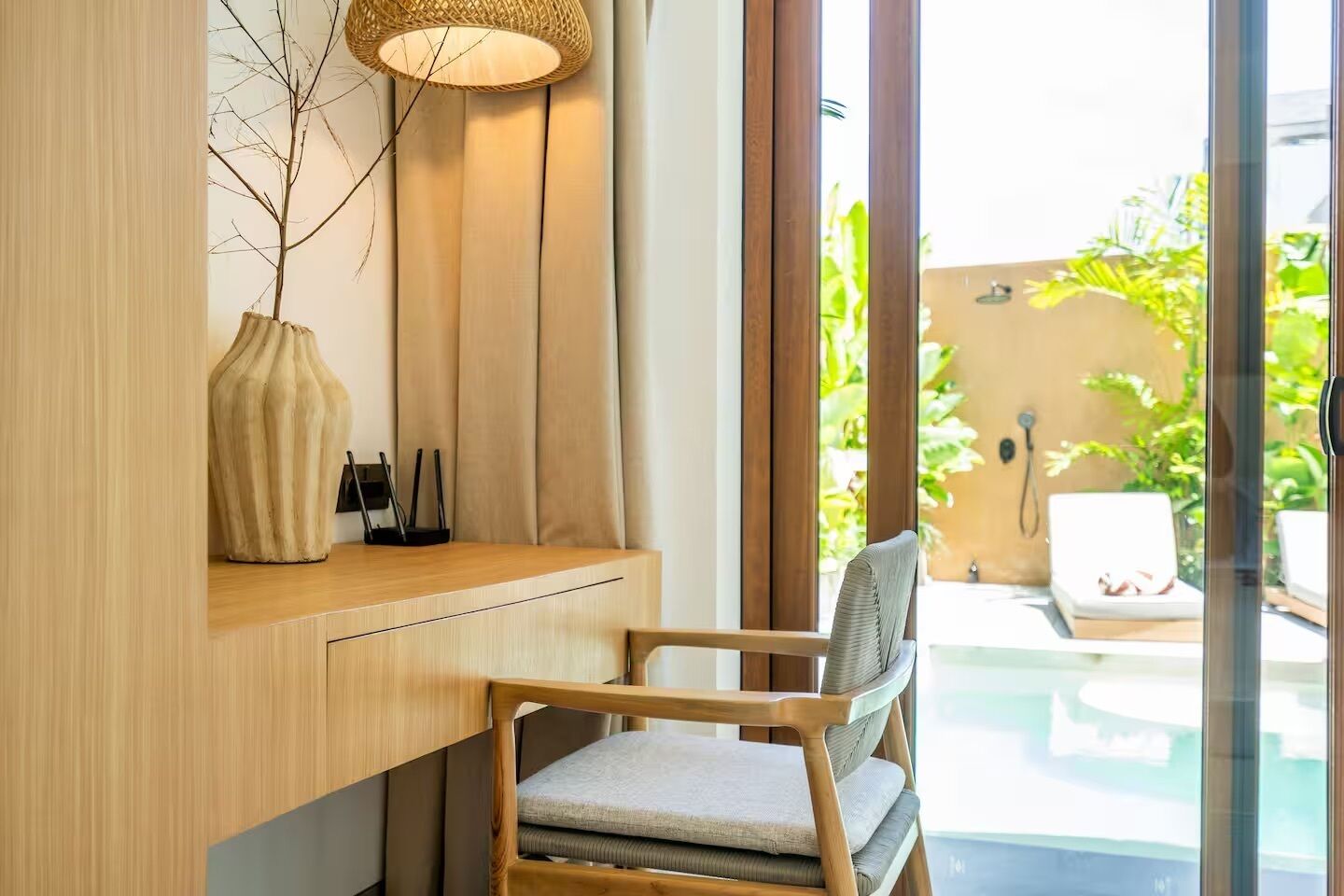 A modern room with a wooden desk, a chair, a vase, and a lamp.