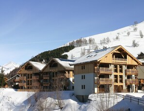 Una cabaña de madera con varios balcones, un telesilla al fondo y una montaña nevada como telón de fondo.