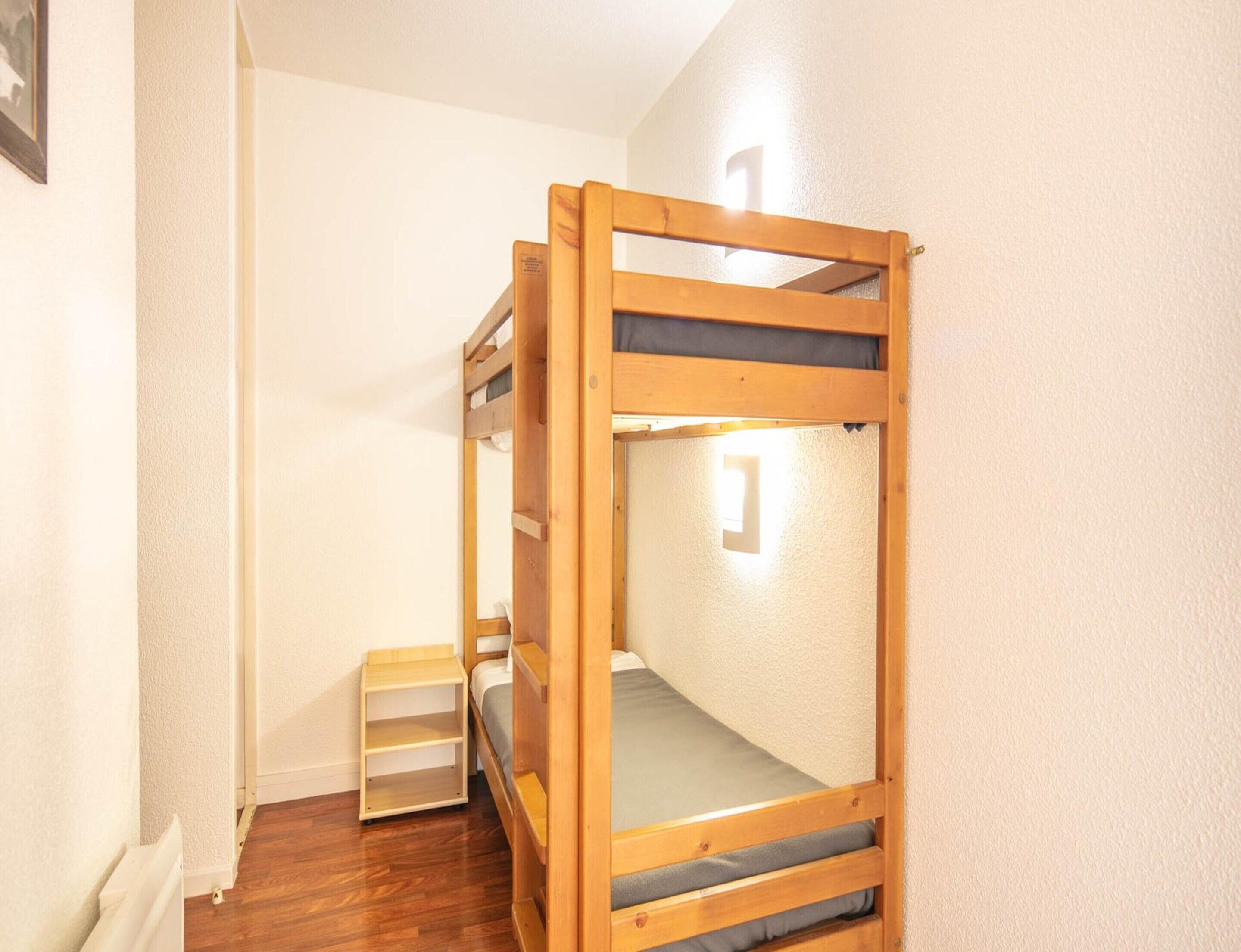 Een stapelbed met houten frame, een klein plankje en een lamp aan de muur.