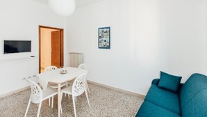 A room with a white table and chairs, a teal sofa, a TV on the wall, and a framed picture.